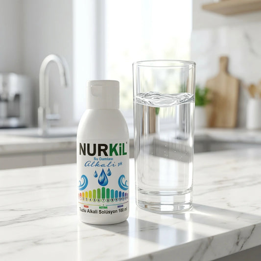Modern mutfak tezgahında bir bardak su yanında sunulan Nurkil alkali pH damlası.